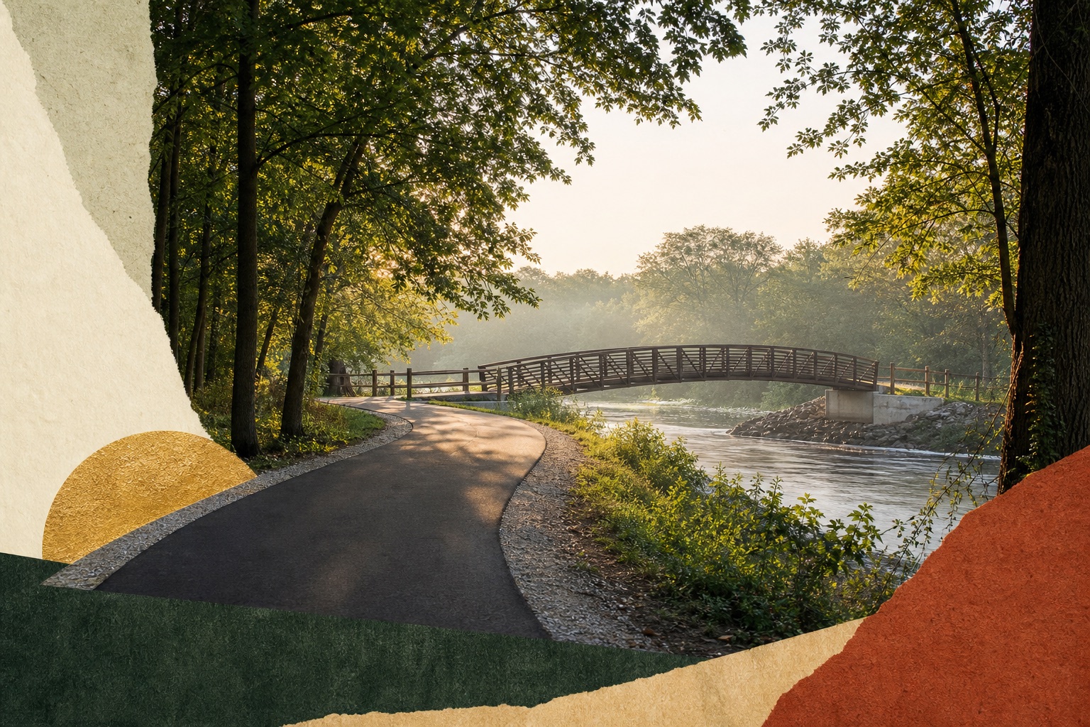 A paved trail curves through mature trees toward a pedestrian bridge over a river.